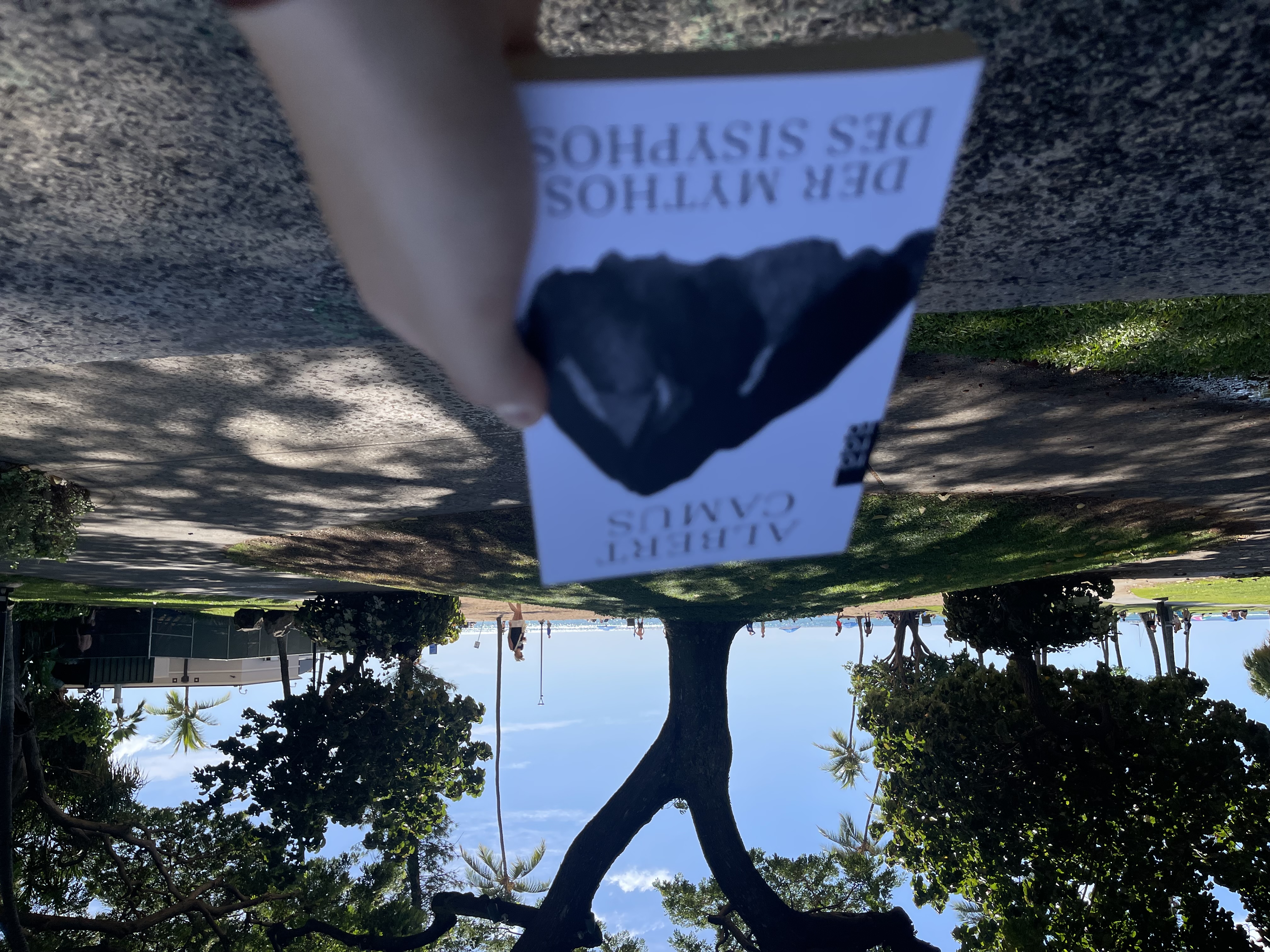 Me holding a German version of 'The Myth of Sisyphus'
          in front of a beach.